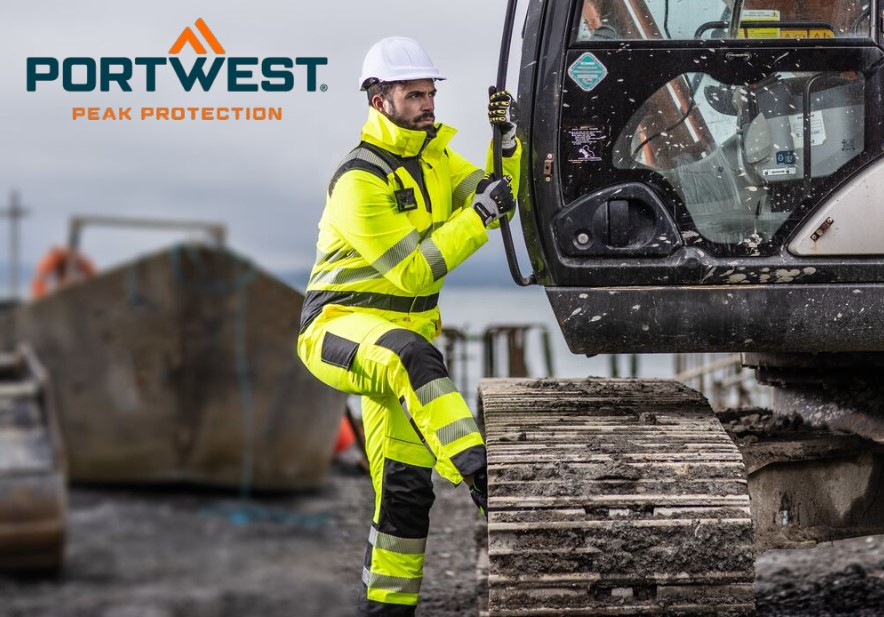 Un trabajador vestido con un traje de alta visibilidad de color amarillo brillante con rayas reflectantes, un casco blanco y guantes se sube a una máquina de construcción. Al fondo se puede ver un entorno de obra con equipos de construcción y un cielo gris. En la parte superior izquierda de la imagen se encuentra el logo de "Portwest" con el lema "Peak Protection". Se proporciona un enlace a nuestra selección de diferentes monos de trabajo.