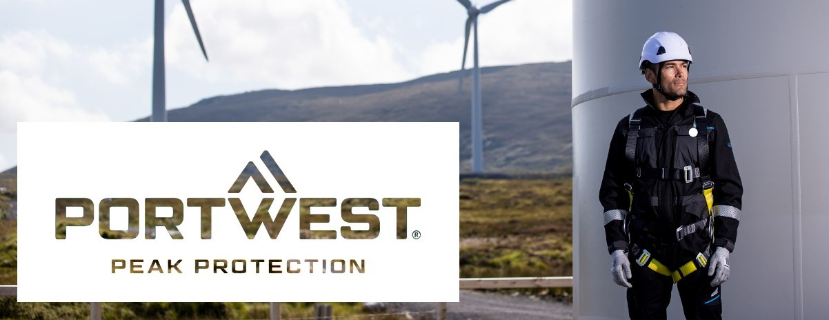 Un trabajador que lleva equipo completo de protección contra caídas se encuentra junto a una turbina eólica. Al fondo se pueden ver más turbinas eólicas. En primer plano se muestra el logotipo de la empresa Portwest con el lema "Peak Protection".